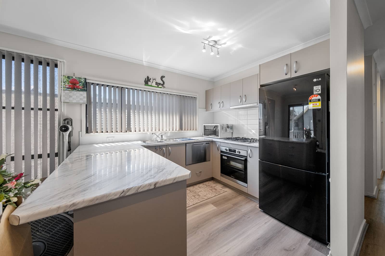 A modern kitchen with a marble-look benchtop, black refrigerator, and light grey cabinetry.