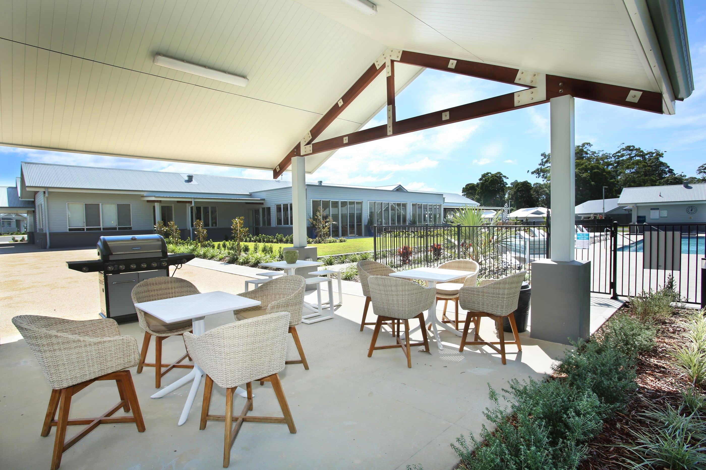 Outdoor patio with tables, chairs, and a barbecue grill next to a swimming pool.