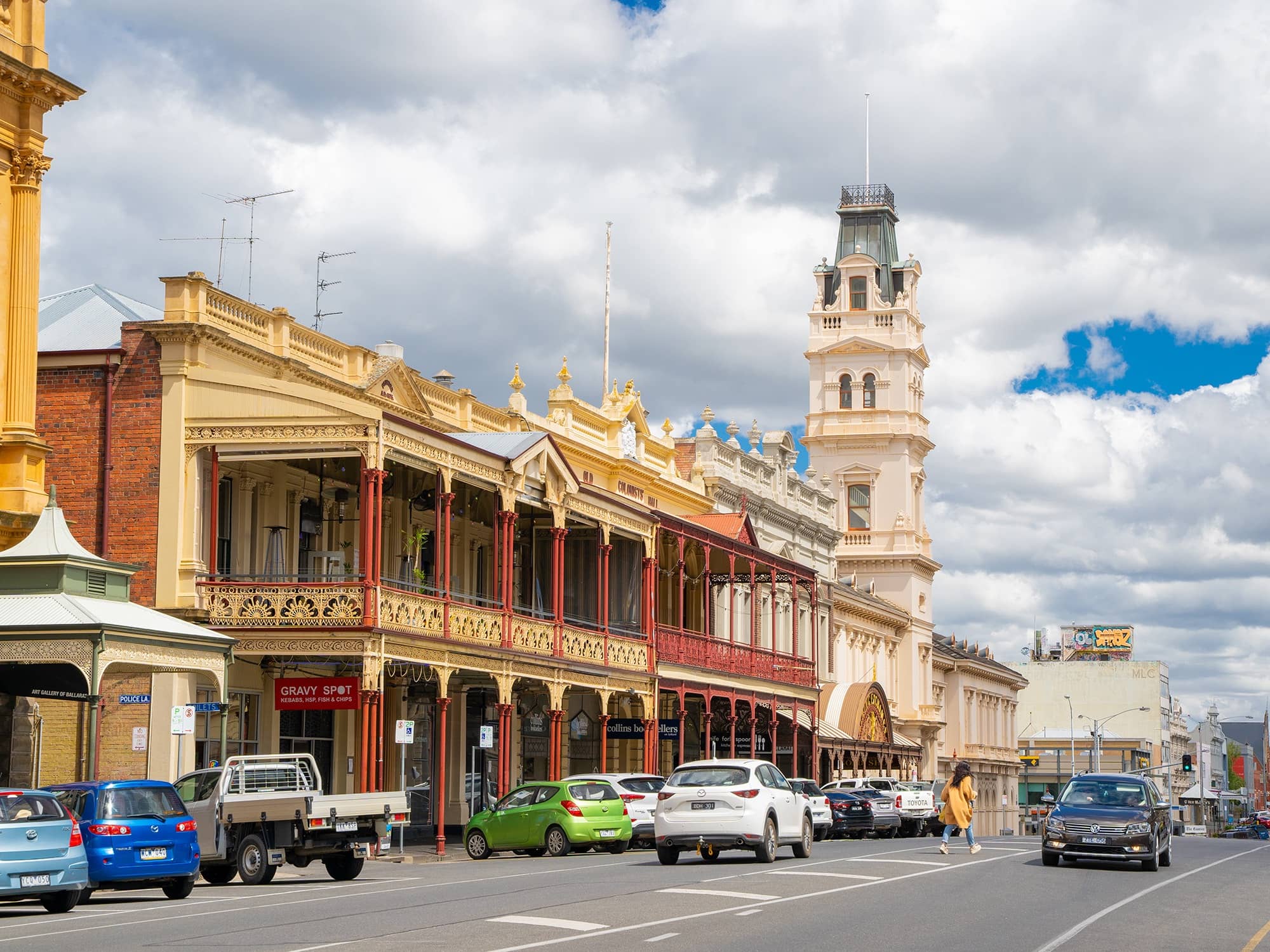 Street scene with heritage buildings and cars under a cloudy sky.