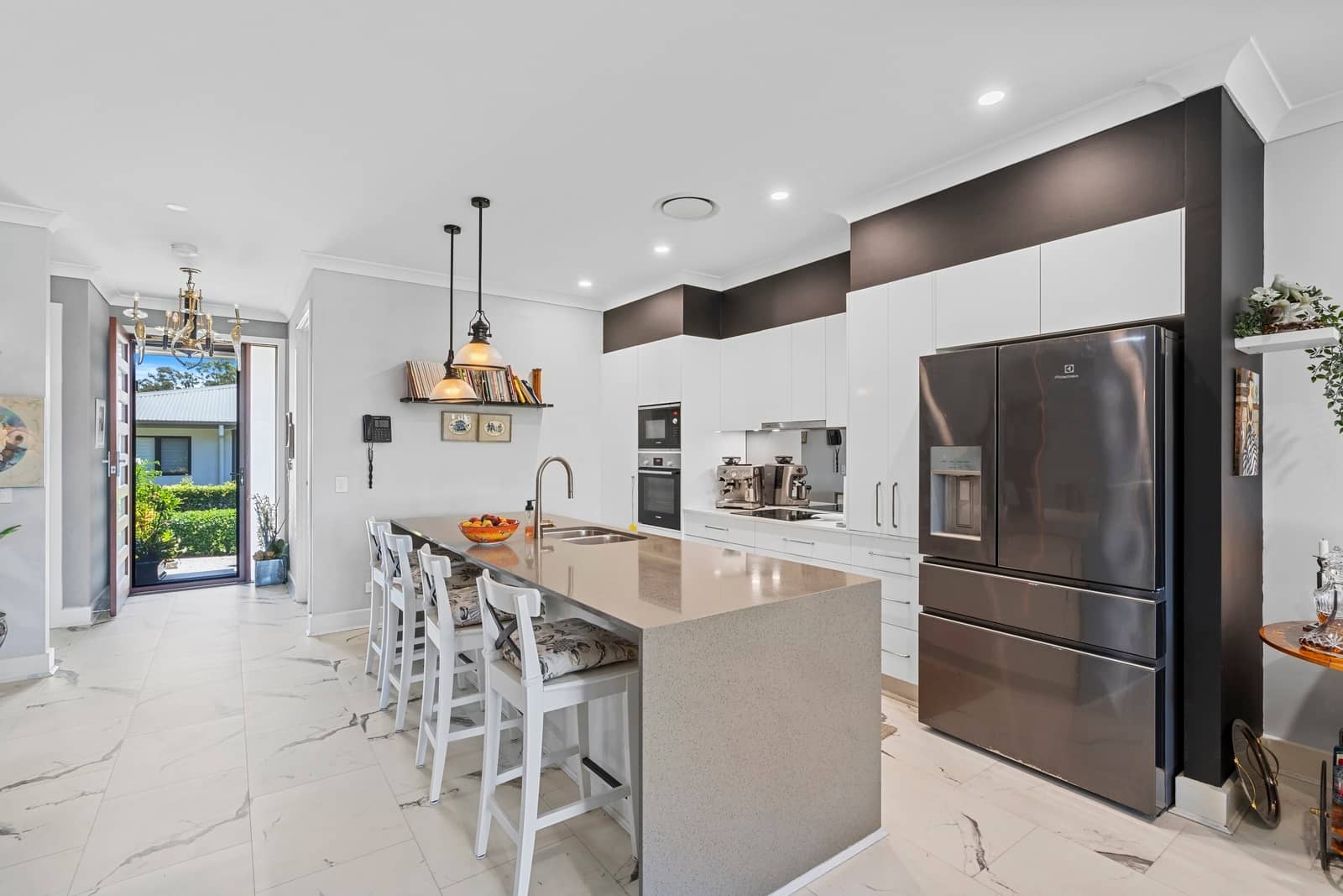 Modern kitchen with island, bar stools, and stainless steel appliances. View to entryway and outside.