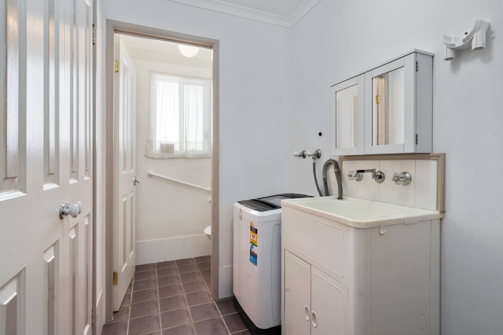 Ingenia Lifestyle home laundry room with washing machine, tub, mirrored cabinet, and tiled floor. Adjoining bathroom has a grab bar.
