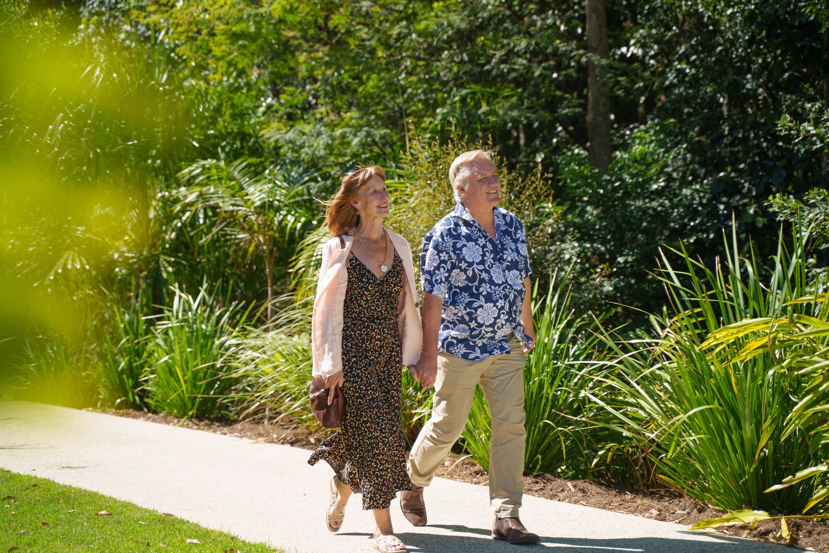 Two people walk on a paved path bordered by lush green plants in an Ingenia Lifestyle community.