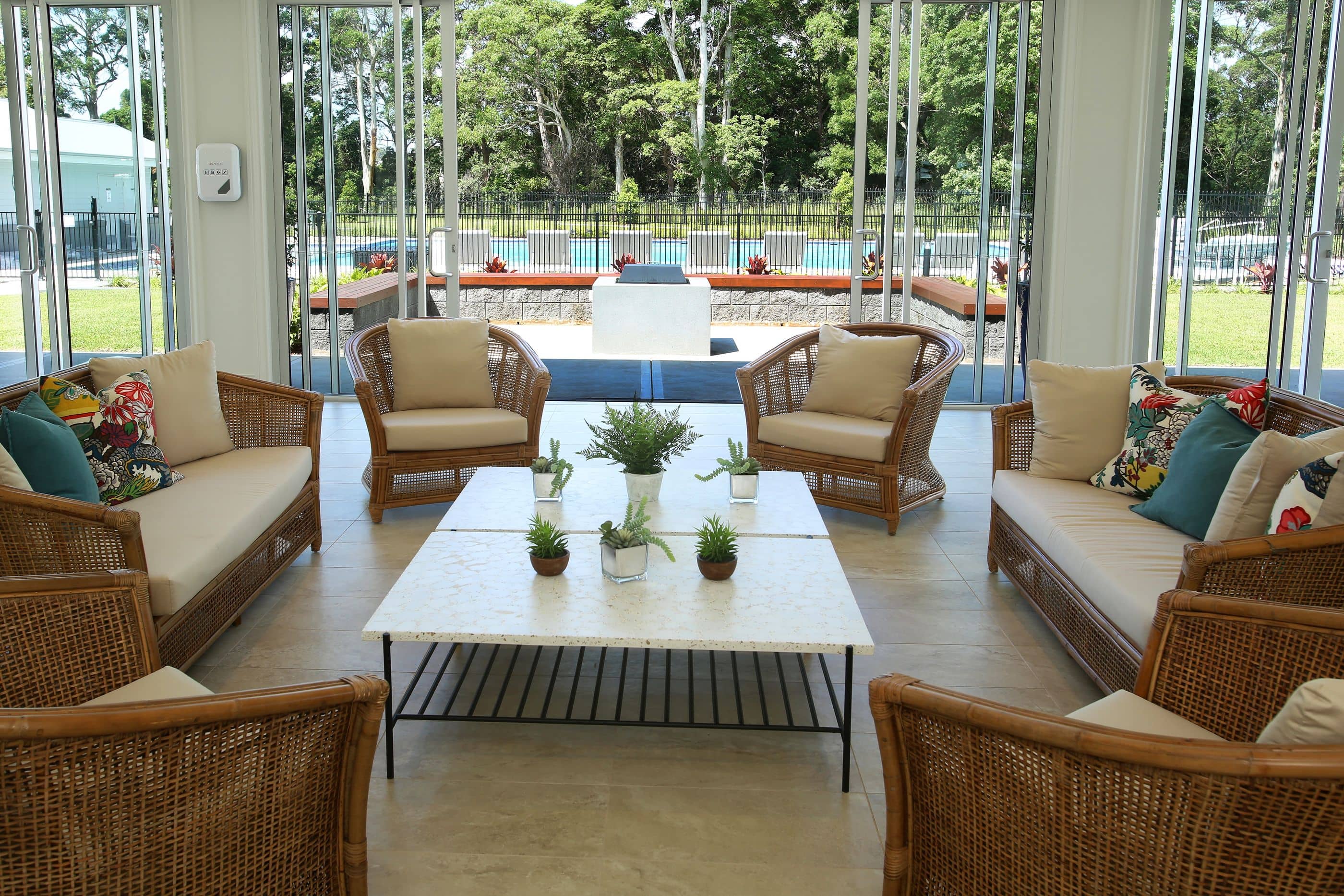 A sunroom with wicker seating and a coffee table overlooks a pool and landscaped grounds.