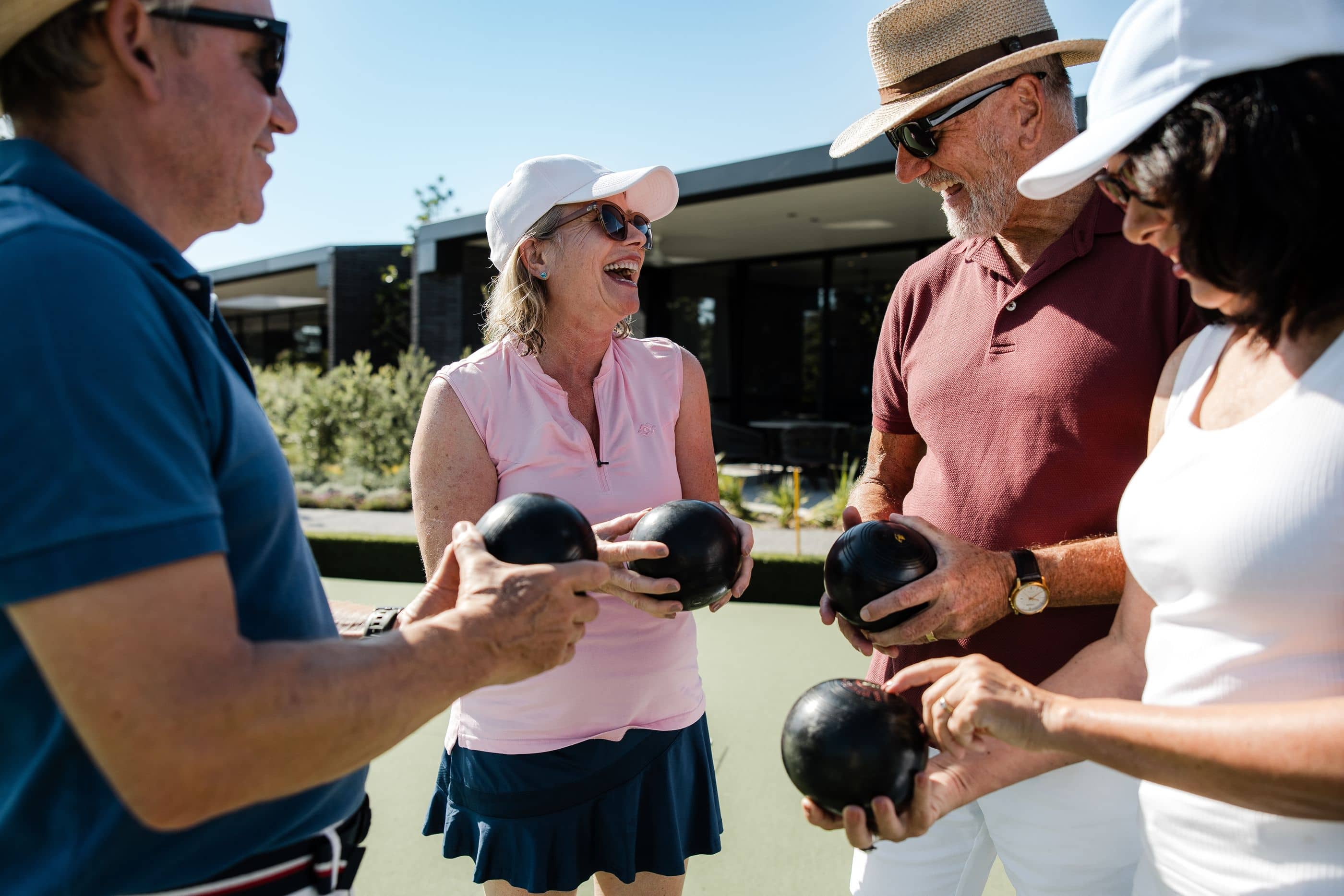 Four people holding lawn bowls on a green with a community building in the background. Ingenia Lifestyle activity.