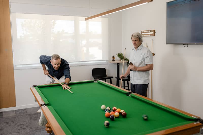 Two men play billiards in a communal recreation room at an Ingenia Lifestyle community.