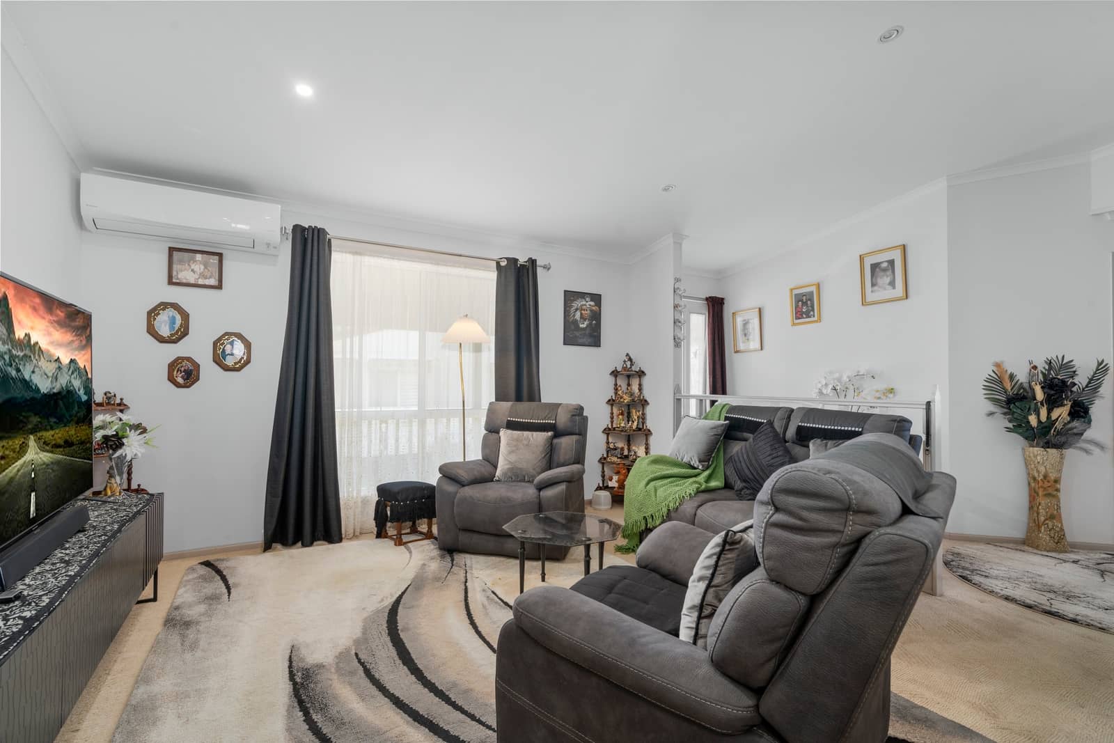 A comfortable living room in an Ingenia Lifestyle home with grey recliners, a TV, and a neutral patterned rug.