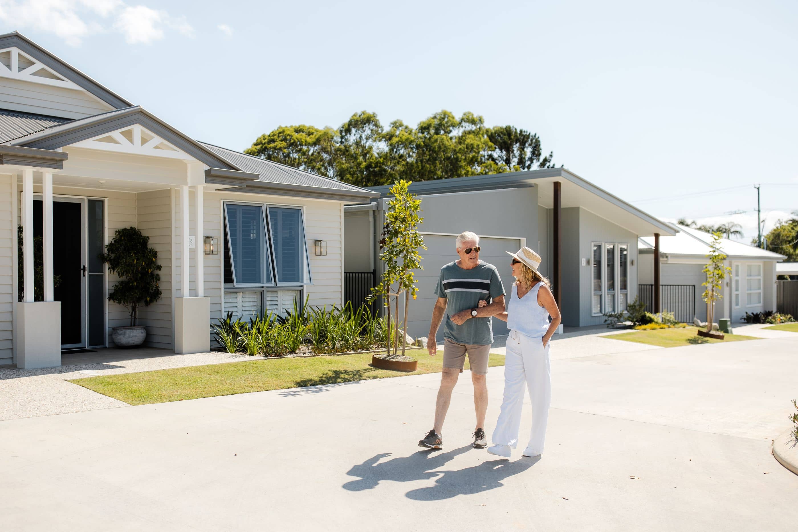 Two residents walk arm-in-arm on a sunny day past modern Ingenia Lifestyle homes and manicured lawns.
