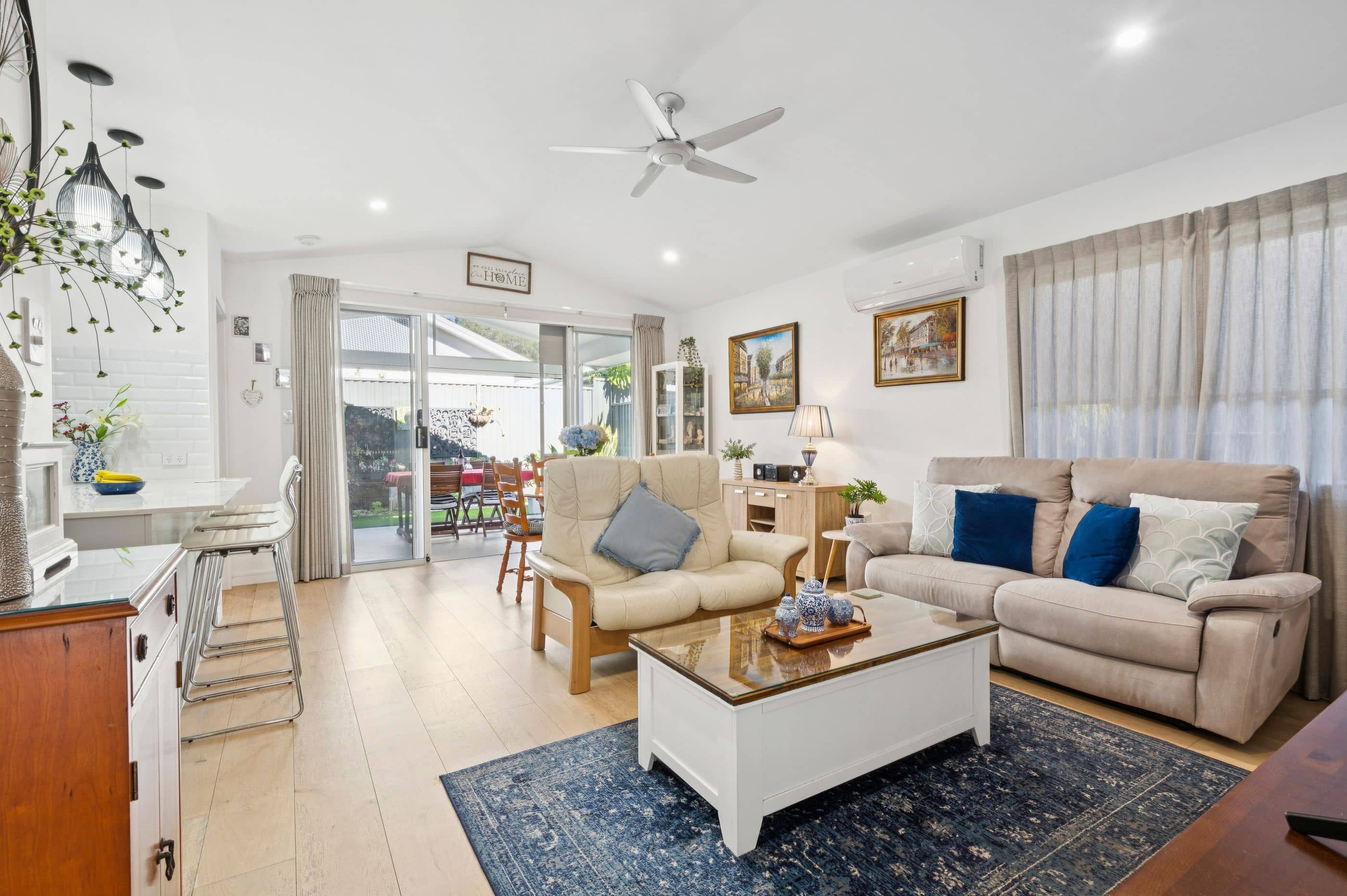 A bright living room with a sofa, armchair, coffee table, and a dining area visible through sliding doors in an Ingenia Lifestyle community.