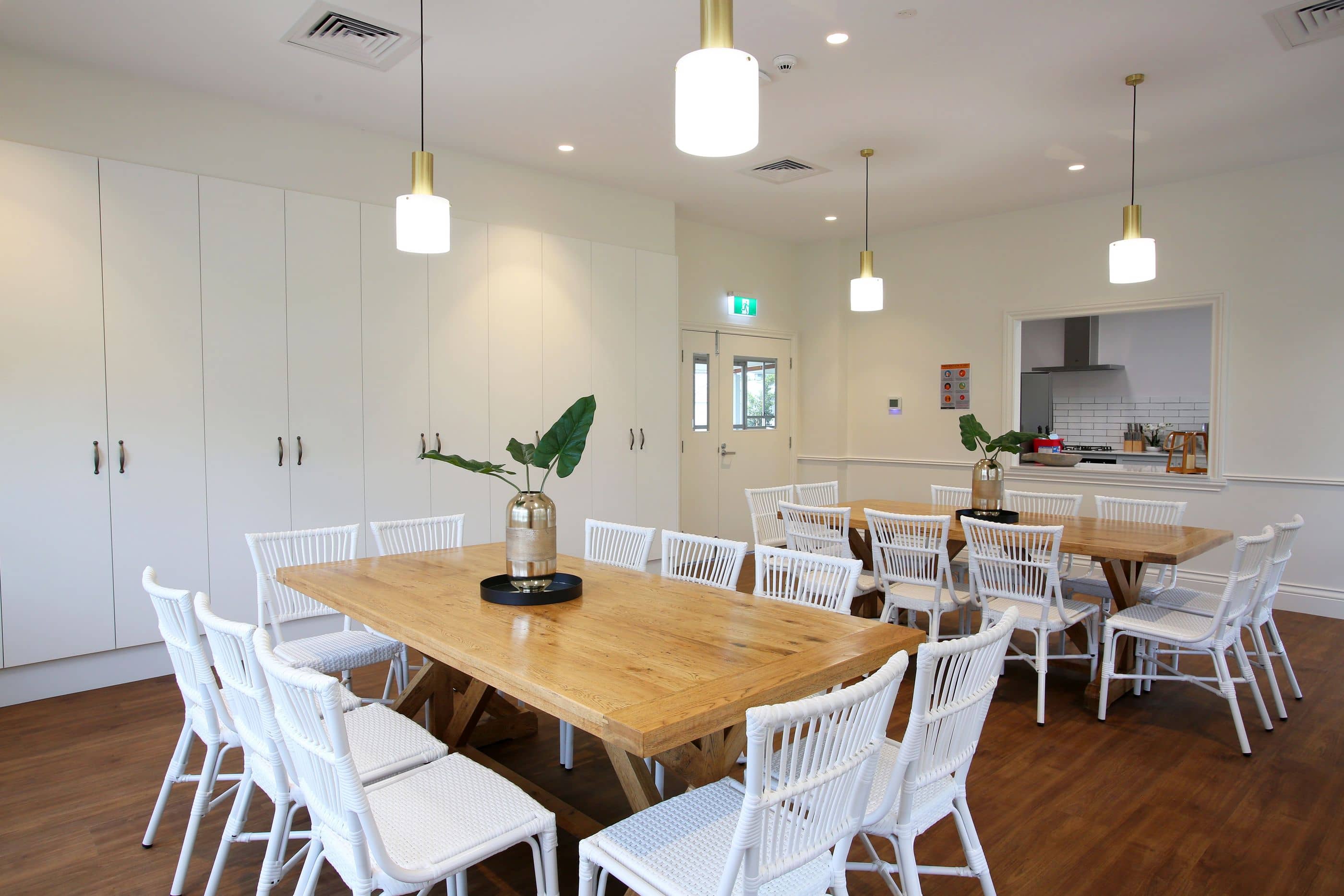 A communal dining area in an Ingenia Lifestyle community featuring two large wooden tables with white chairs, and built-in storage.