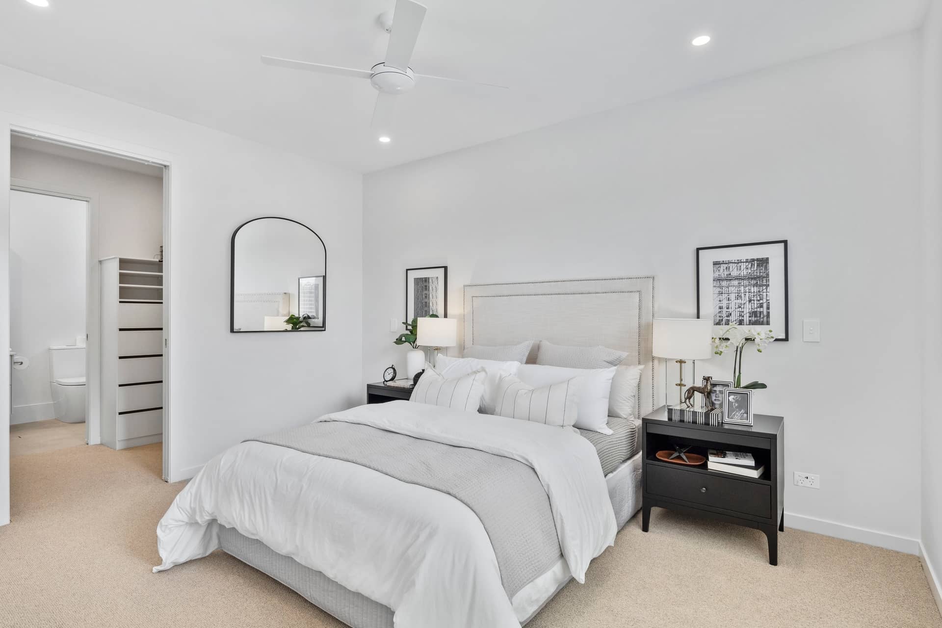 Bedroom with a queen-size bed, white bedding, grey throw, and bedside tables. A ceiling fan is visible.