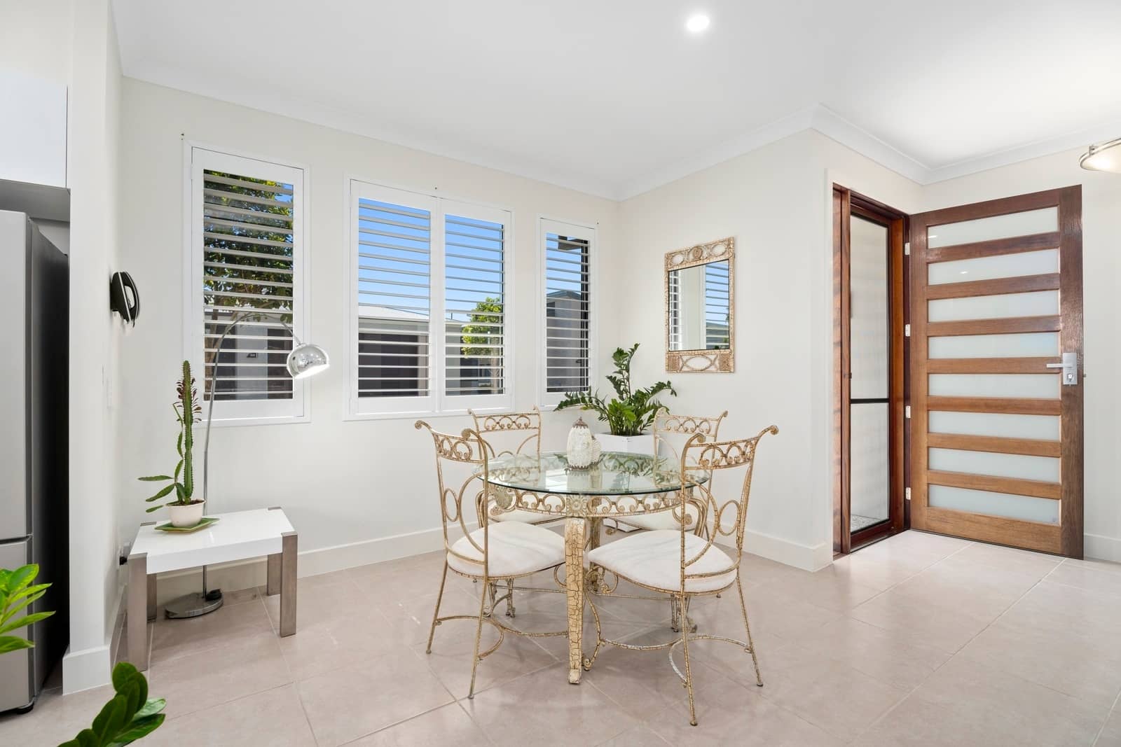 Open-plan dining area in an Ingenia Lifestyle home with a glass table, ornate chairs, and shuttered windows overlooking the community.