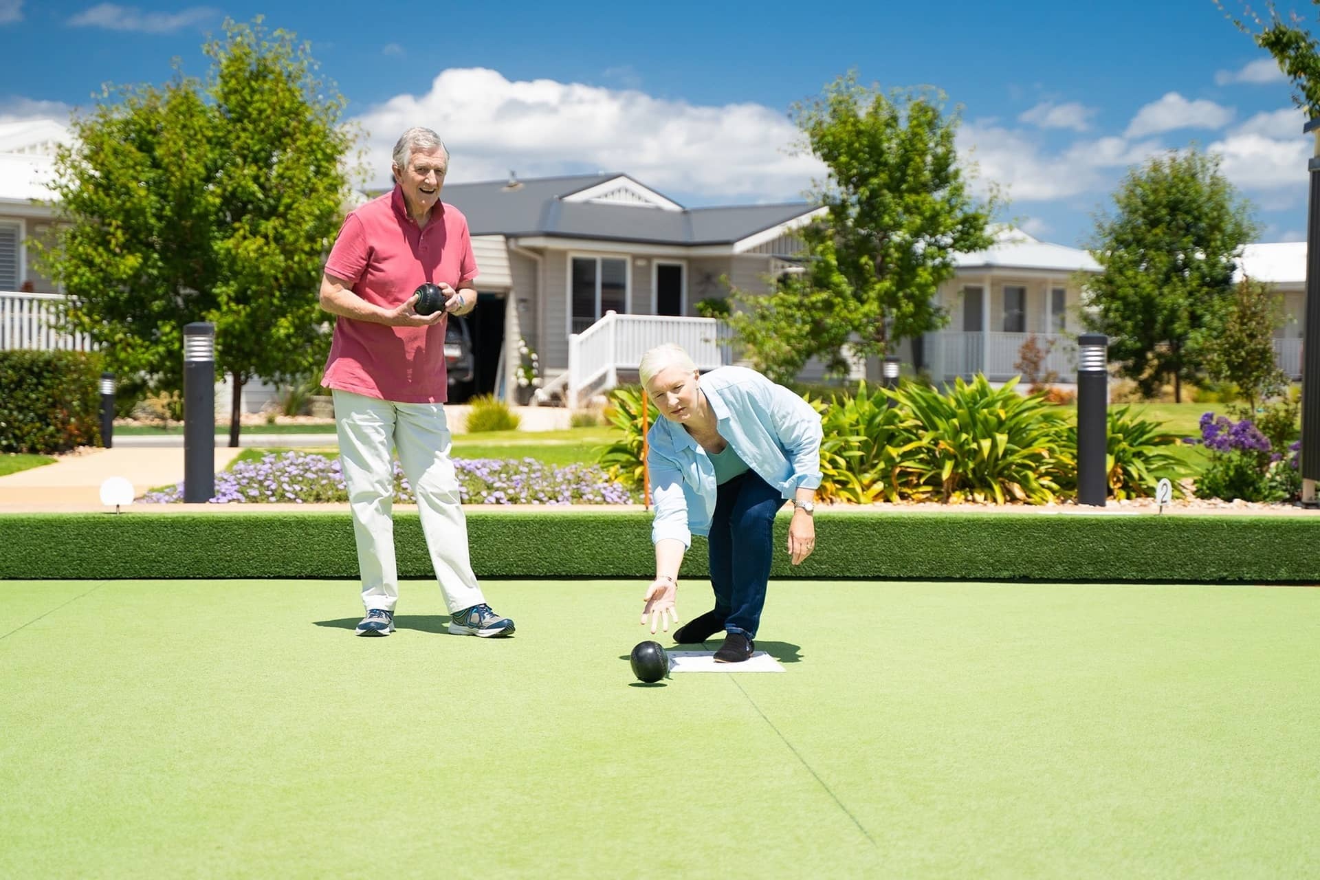 Two people play lawn bowls on a green in an Ingenia Lifestyle community, with homes in the background.