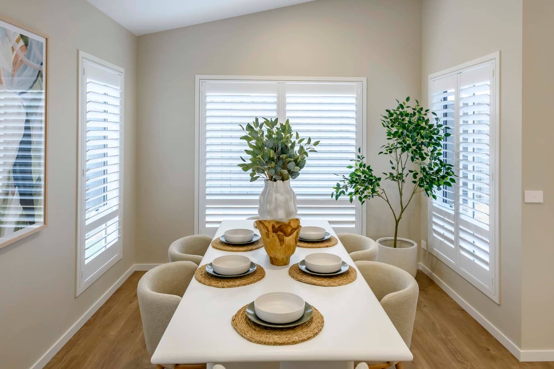 A dining table set with plates and a decorative vase in a room with plantation shutters.