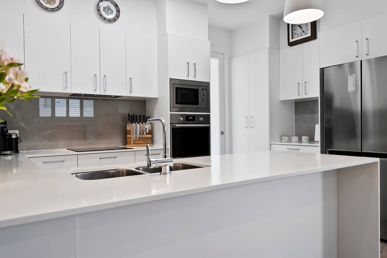 A bright, modern kitchen in an Ingenia Lifestyle home with white cabinets, light stone benchtops, a large island with sink, and integrated appliances.