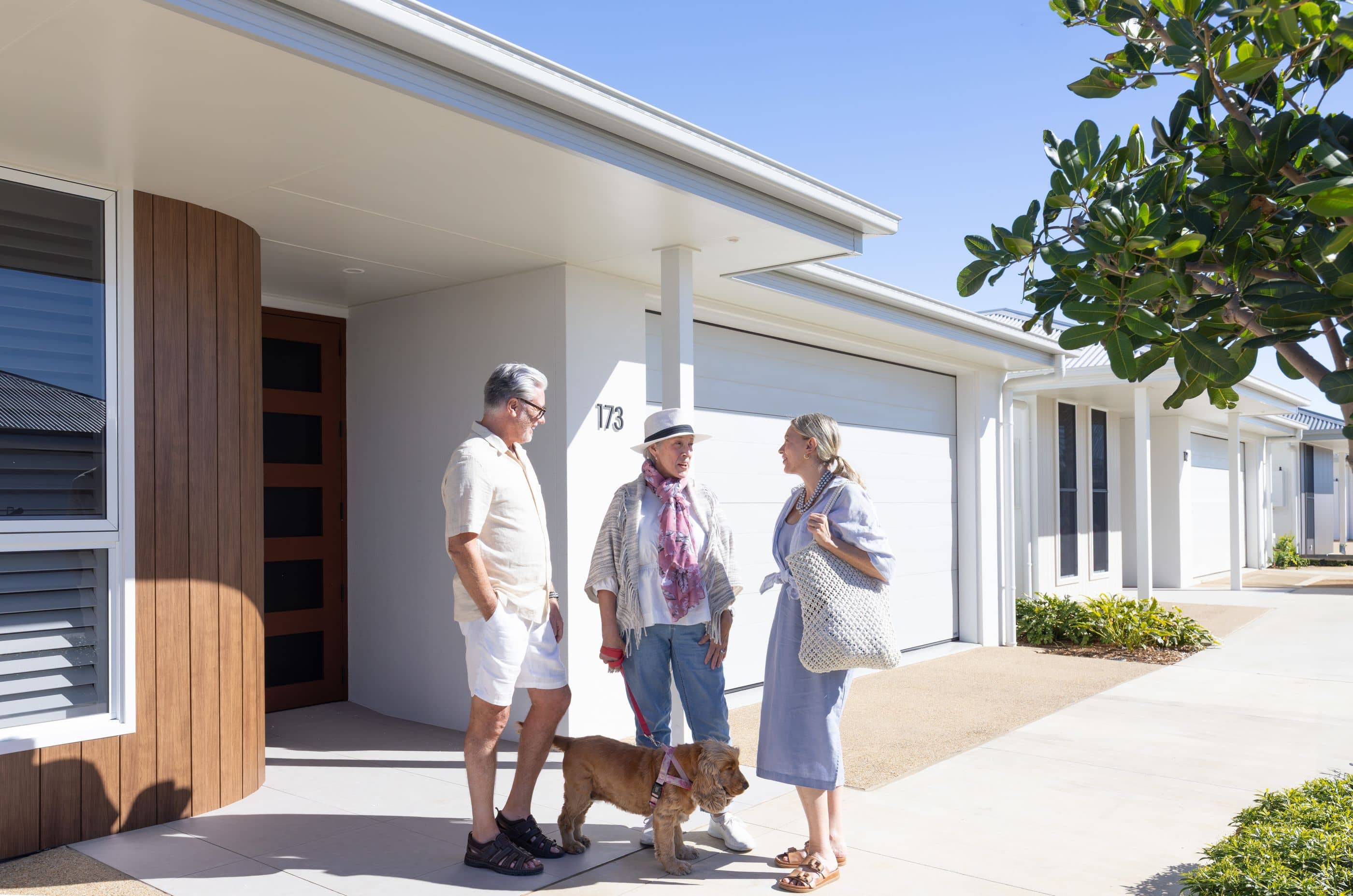 Three people and a dog stand outside modern land lease homes in an Ingenia Lifestyle community.