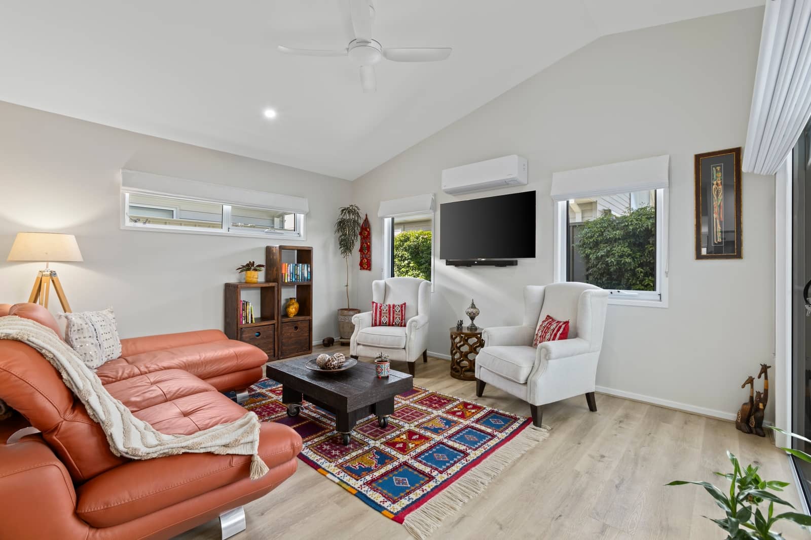A modern living room with a leather sofa, two armchairs, a dark wood coffee table, and a colorful rug.