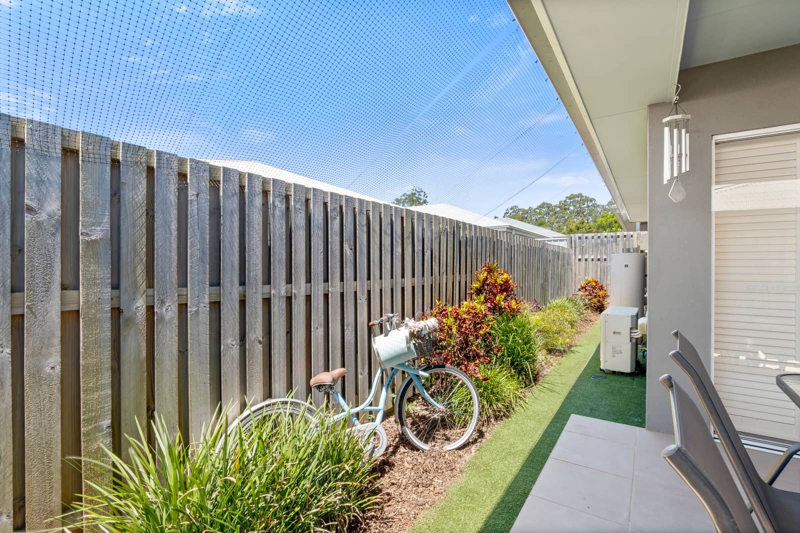 A light blue bicycle with a basket stands near a wooden fence in an Ingenia Lifestyle community yard.