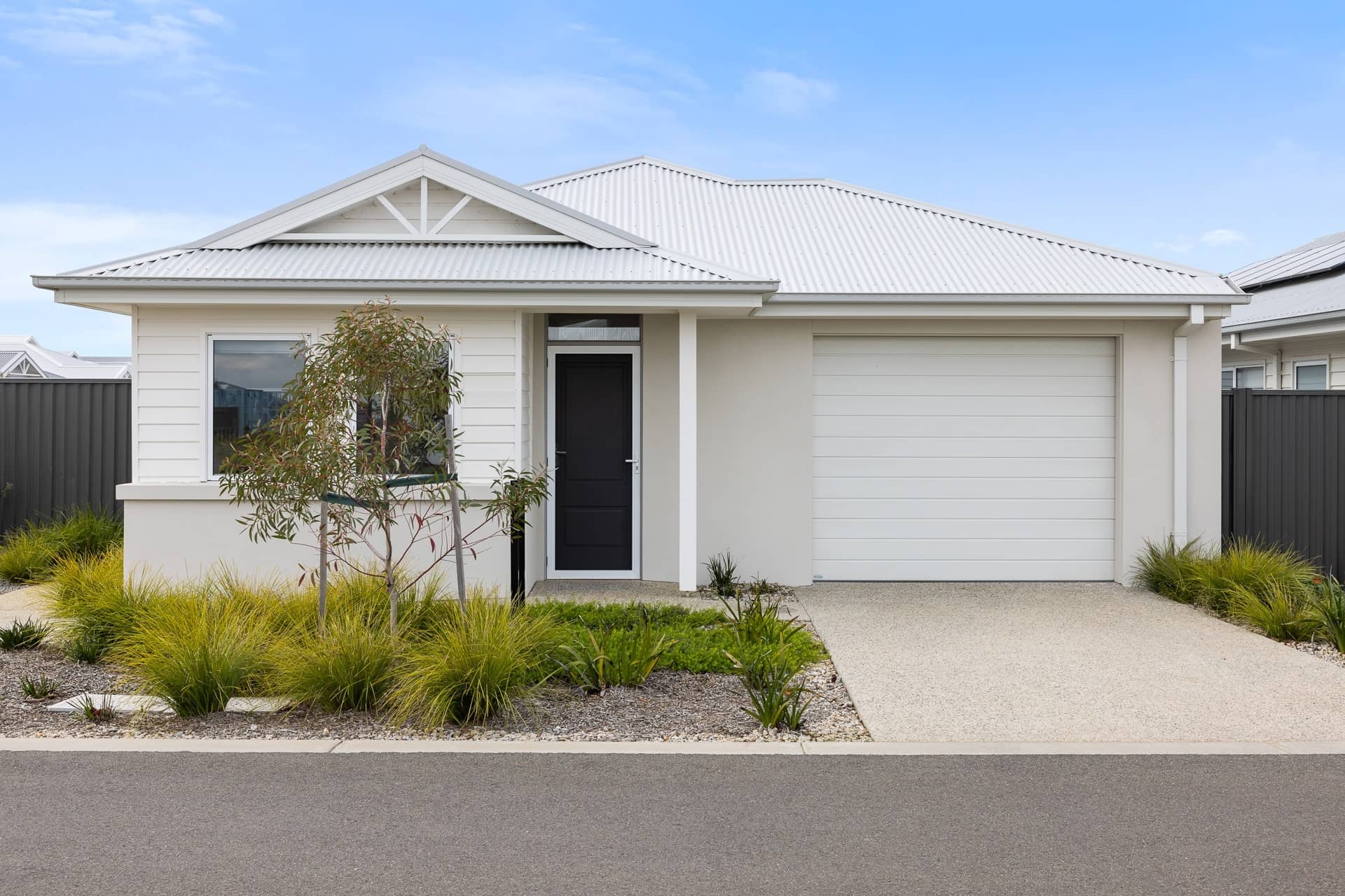 Modern Ingenia Lifestyle home with white corrugated roof and garage, low-maintenance landscaping.