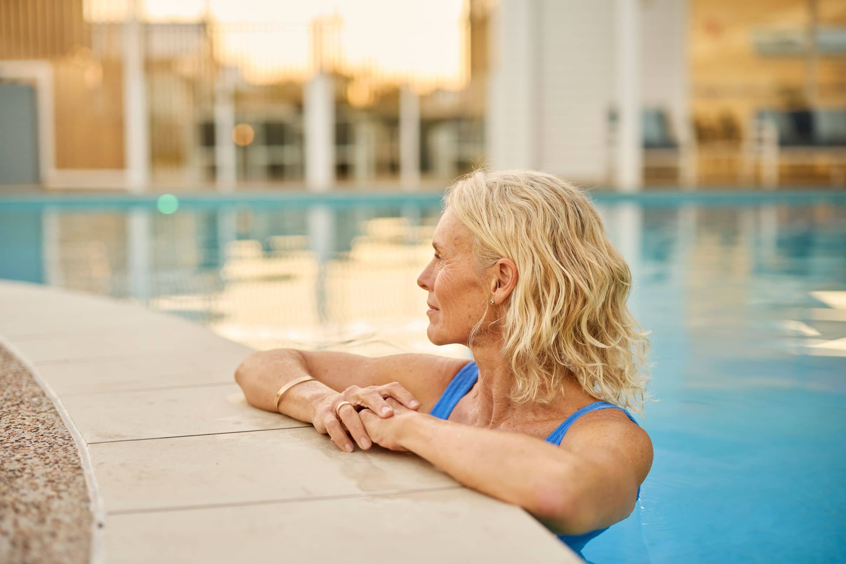 Woman leaning on edge of a bright blue swimming pool, looking to the left.
