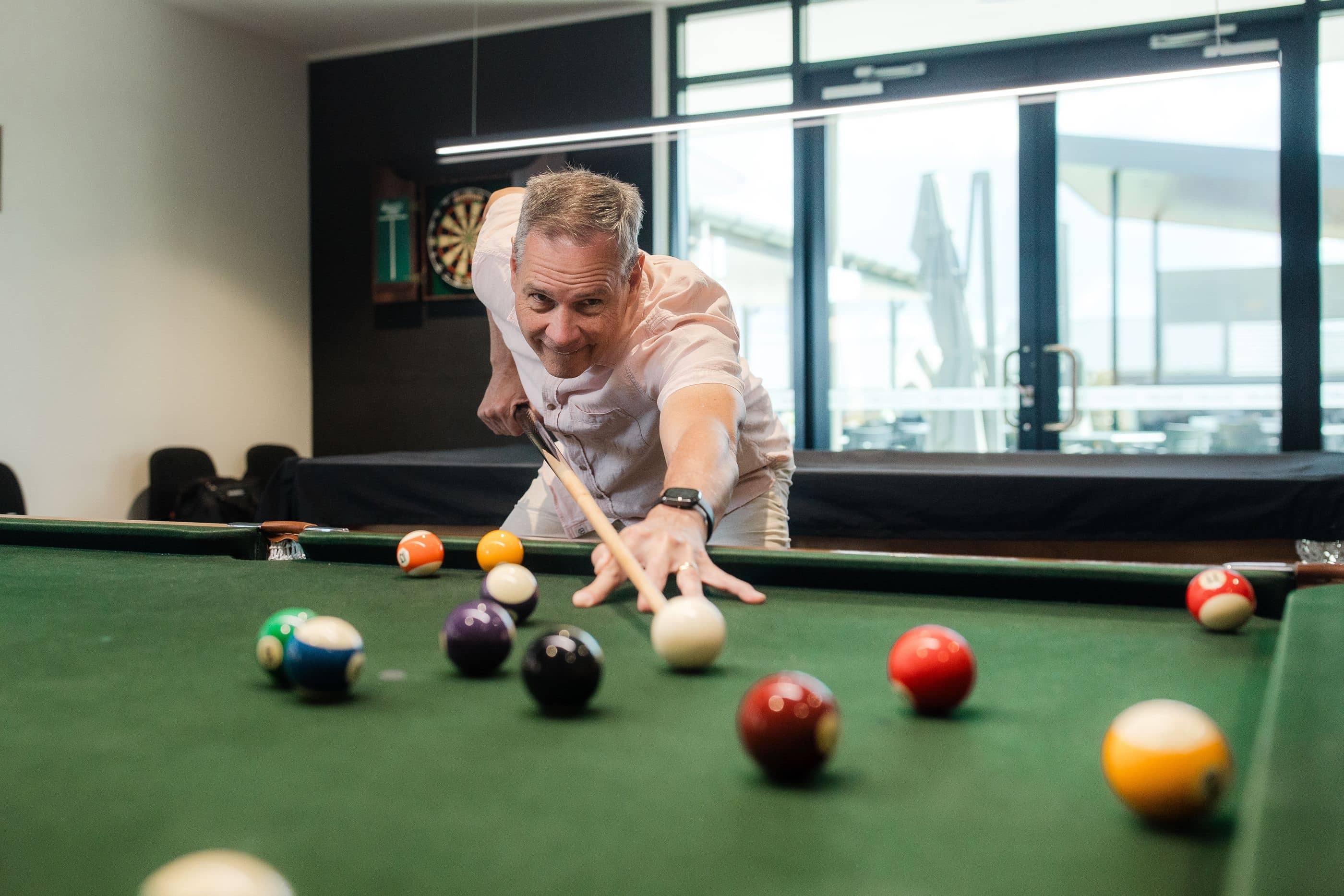 Man playing billiards on a green table in an Ingenia Lifestyle shared amenities room, smiling as he takes a shot.