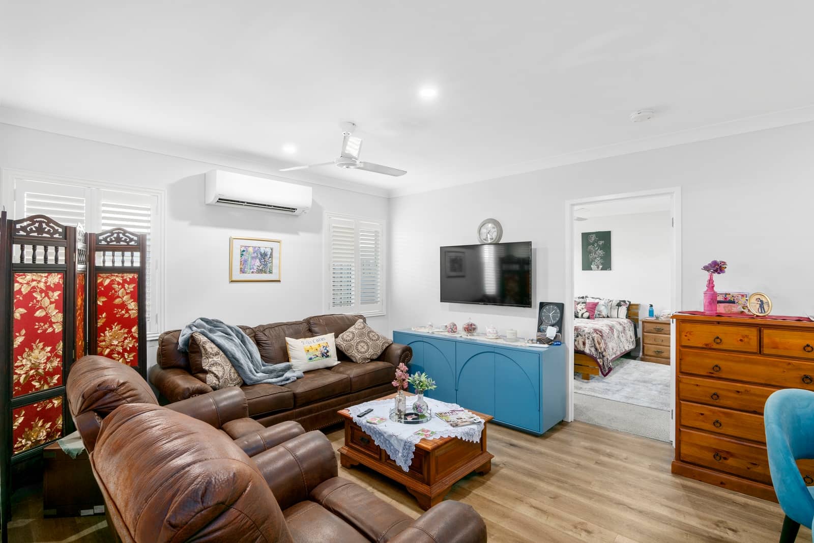 A brown leather lounge suite is in a living room with a TV and a blue cabinet.