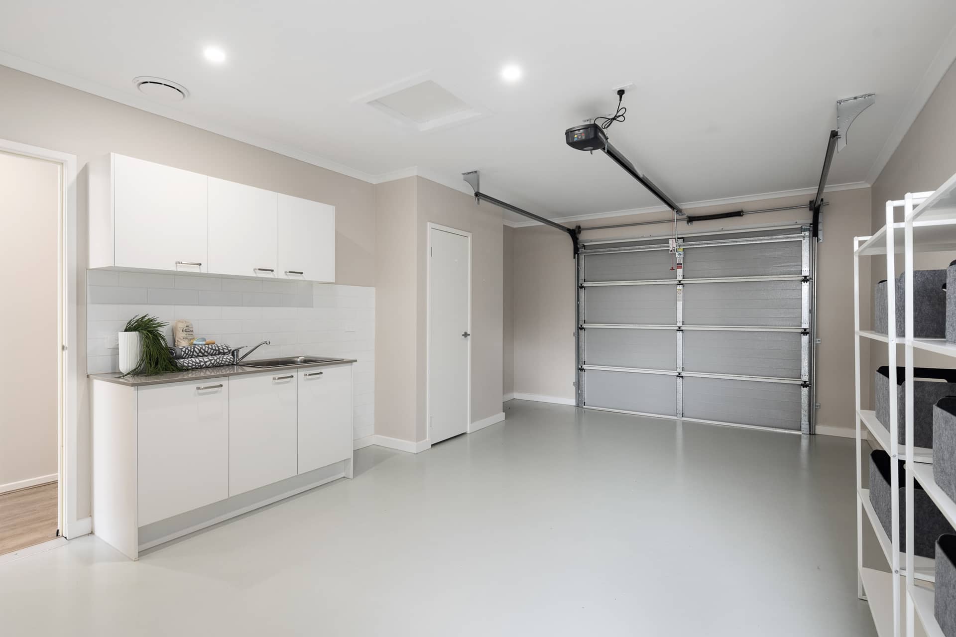 Interior view of a garage with a roller door, laundry cabinets, and shelving.