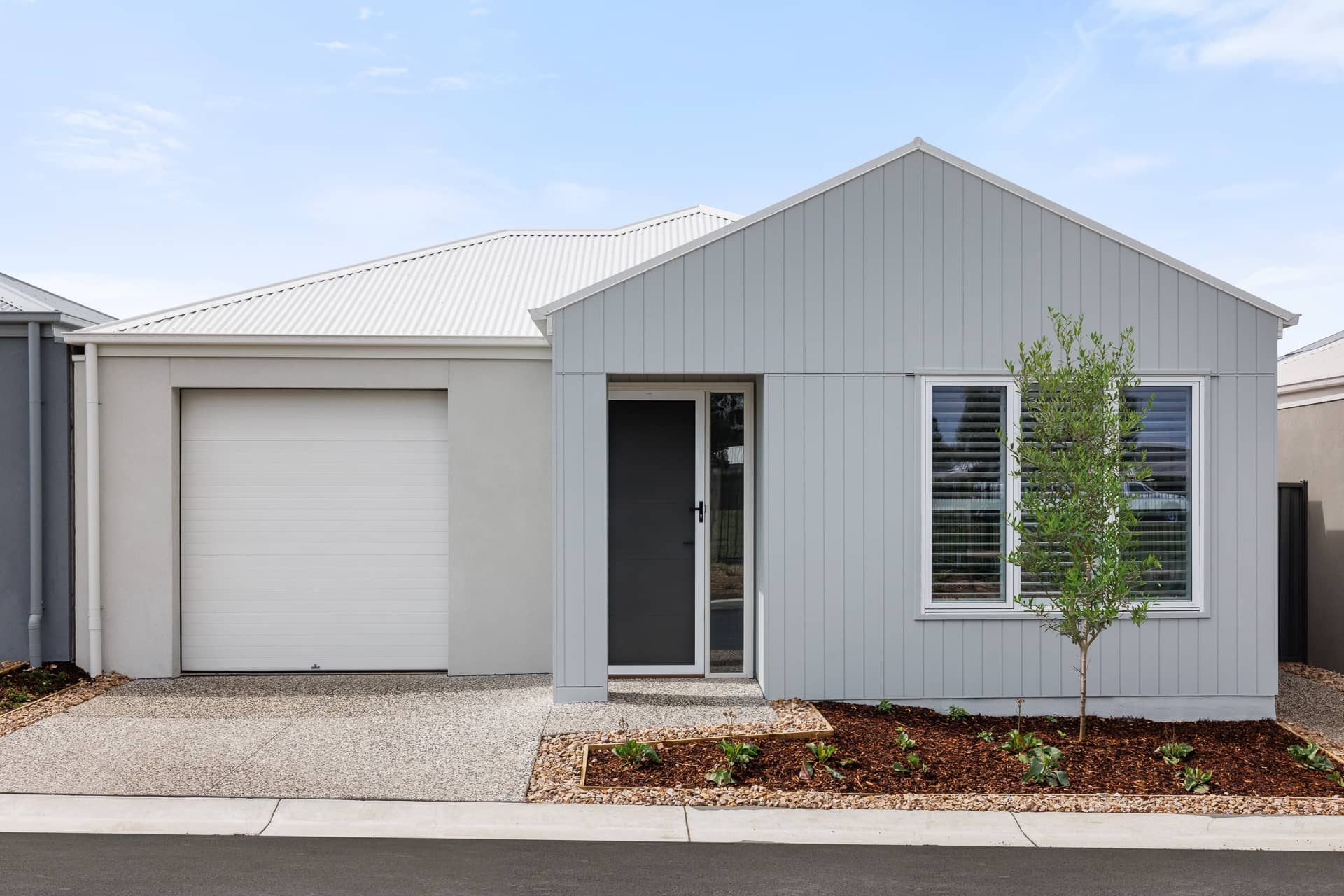 Light grey Ingenia Lifestyle home with a garage, front door, and low-maintenance landscaped garden bed.