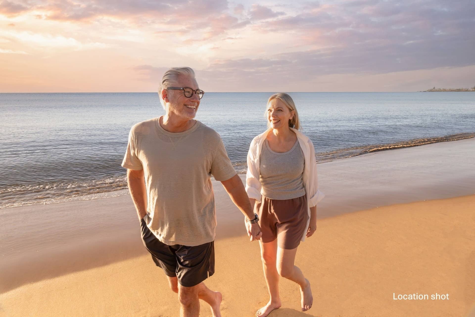 A man and a woman walk hand-in-hand on a sandy beach at sunset.