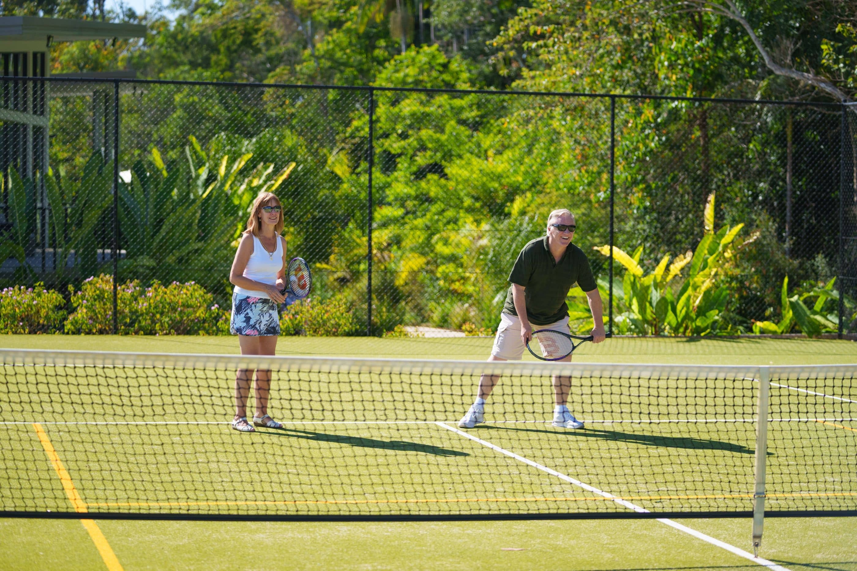 Two people on a tennis court with rackets and green foliage. Enjoying active living at an Ingenia Lifestyle community.