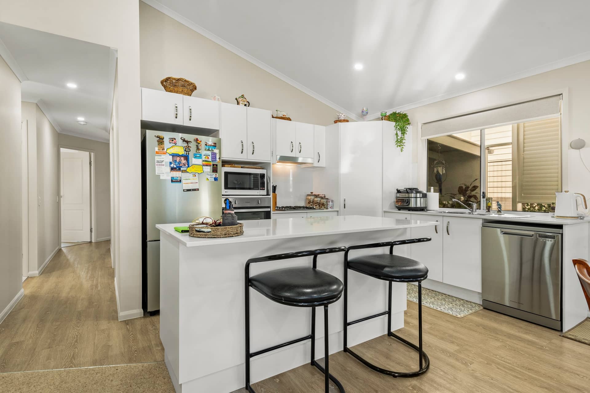 Modern kitchen in an Ingenia Lifestyle home with white cabinets, stainless steel appliances, a kitchen island, and wood-look flooring.