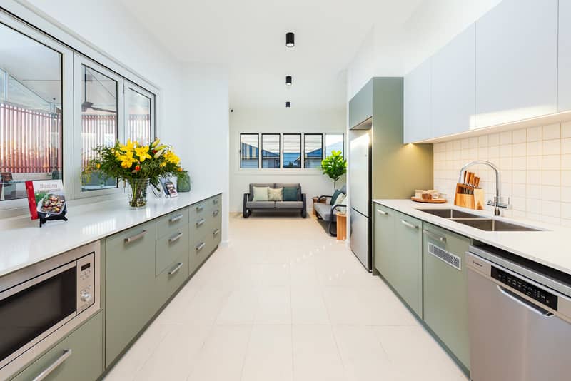 Modern kitchen with light green cabinetry, stainless steel appliances, and a seating area in the background.