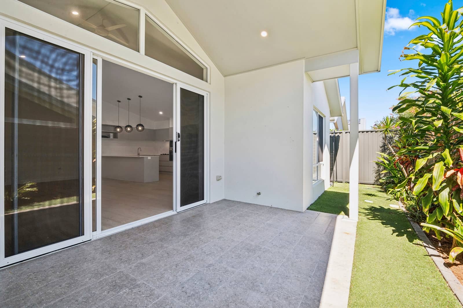 Modern patio overlooking a kitchen, with sliding glass doors and lush garden views.