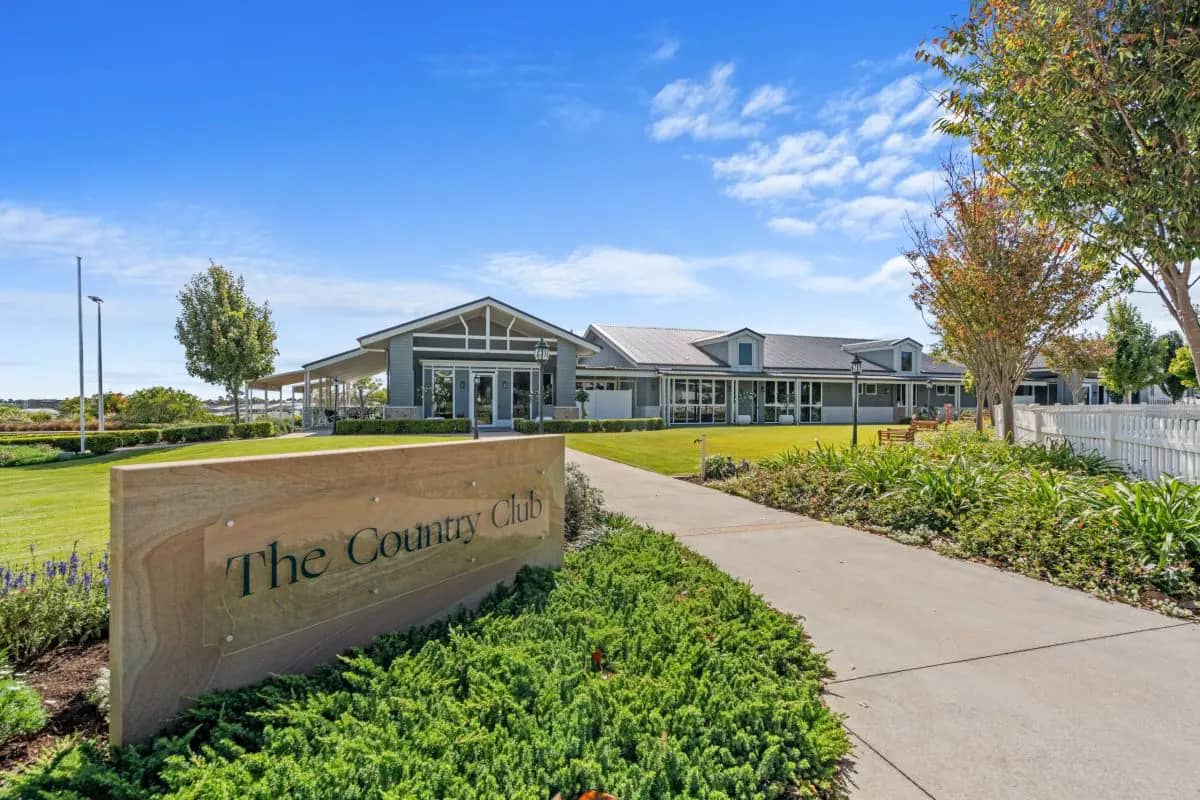 Stone sign for "The Country Club" with a modern grey community building, lawns, and landscaping at Ingenia Lifestyle.