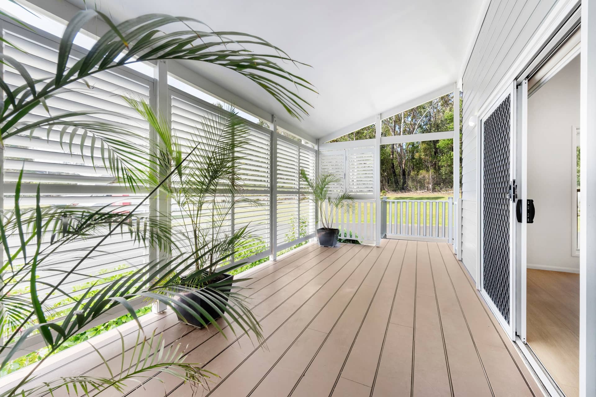 Covered outdoor verandah with louvered screens, deck, potted plants, and sliding door to an Ingenia Lifestyle home.