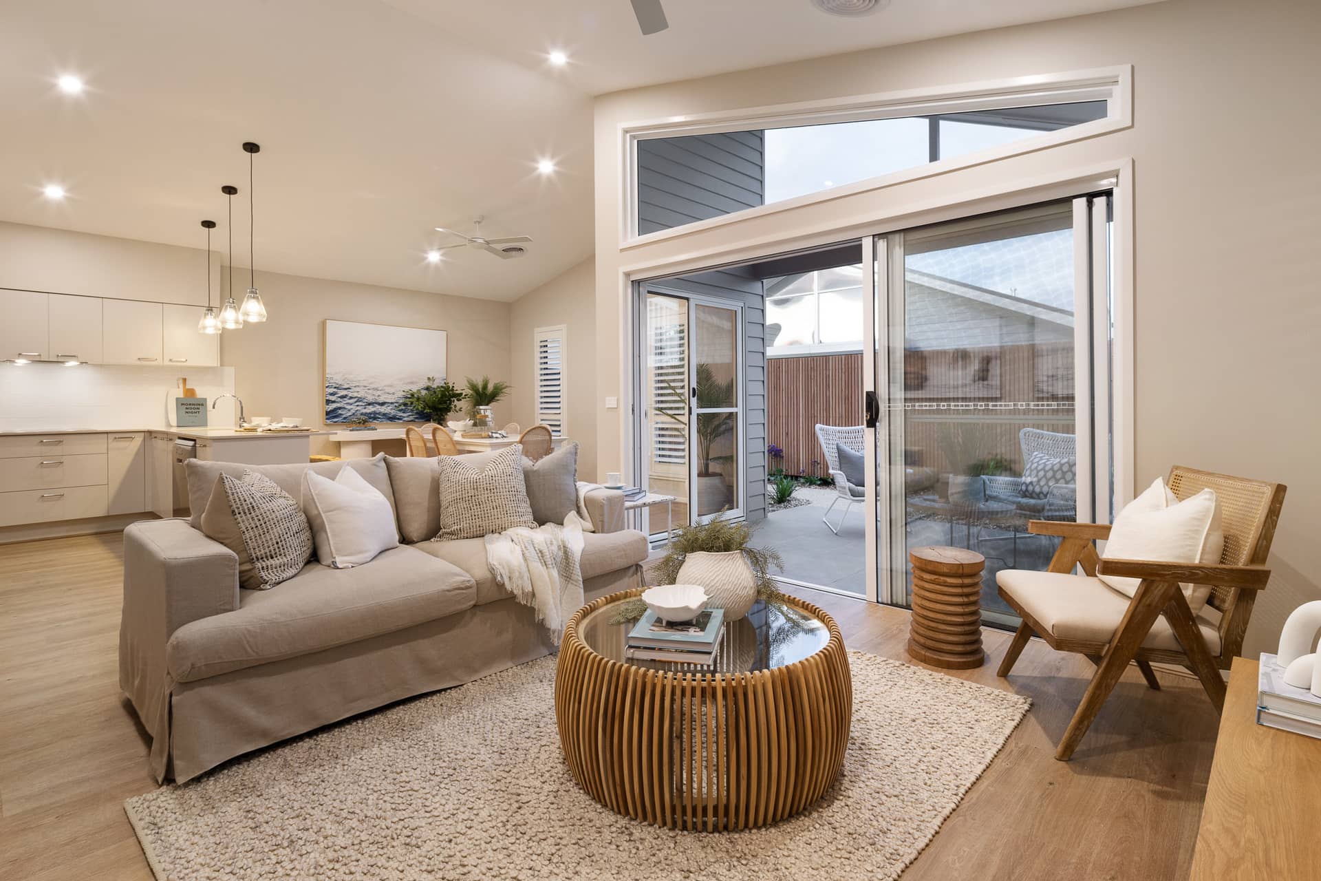 A light-filled open plan living area with a large sofa, coffee table, and kitchen.