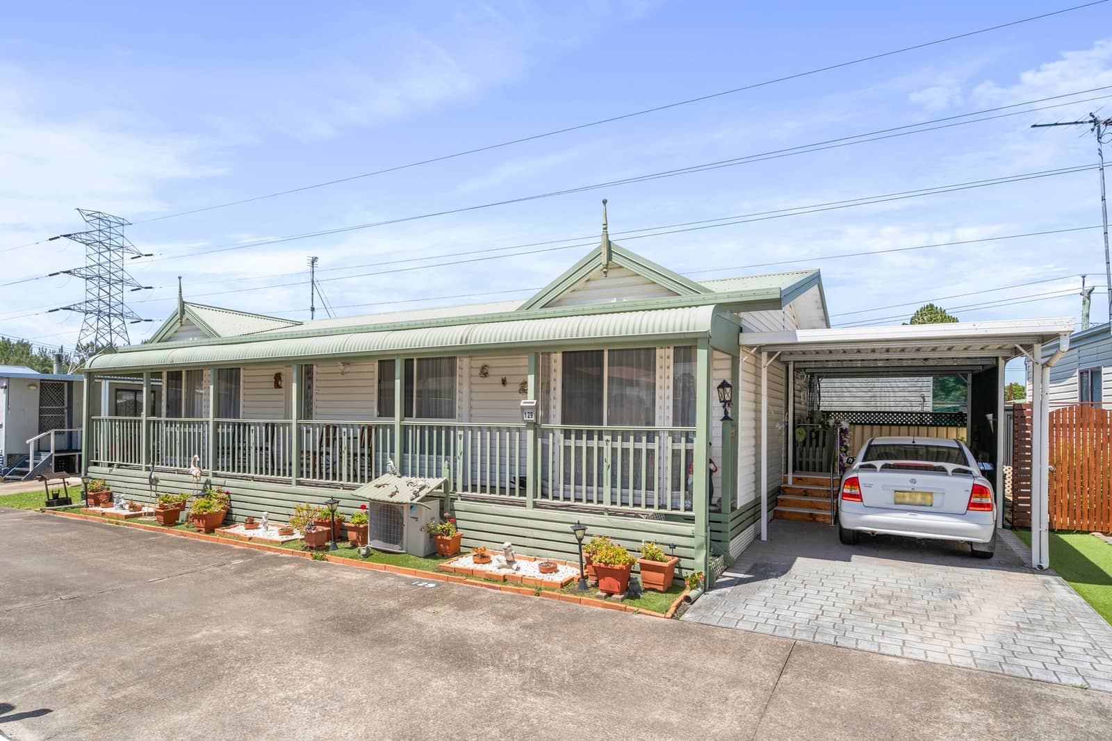 An off-white land lease home with a green porch, carport with a car, and landscaped garden beds at an Ingenia Lifestyle community.