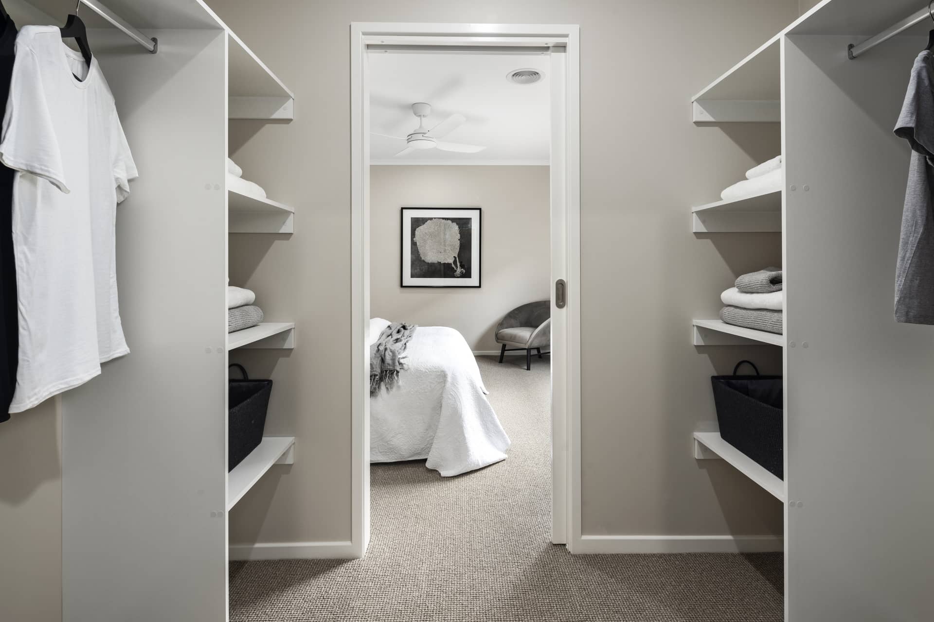 View through a doorway into a bedroom, framed by open closets filled with clothes and folded linens.