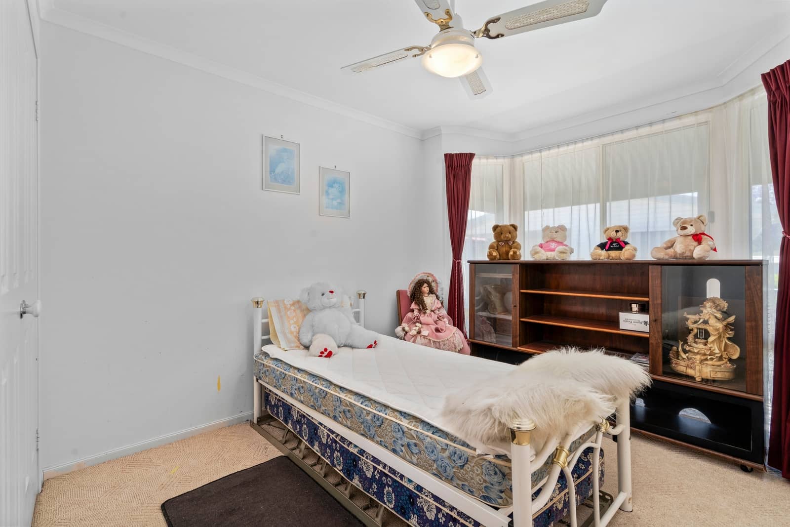 Bedroom with a single bed, bay window, white walls, and a wooden display cabinet in an Ingenia Lifestyle home.