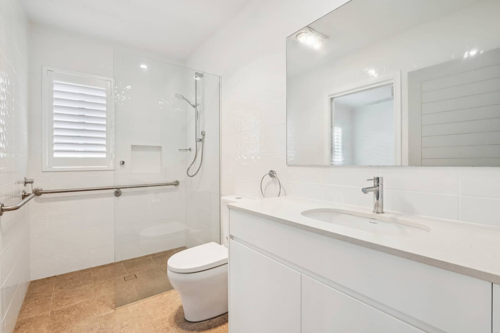 A modern, accessible bathroom in an Ingenia Lifestyle community featuring a toilet, shower with glass screen, and vanity with mirror.