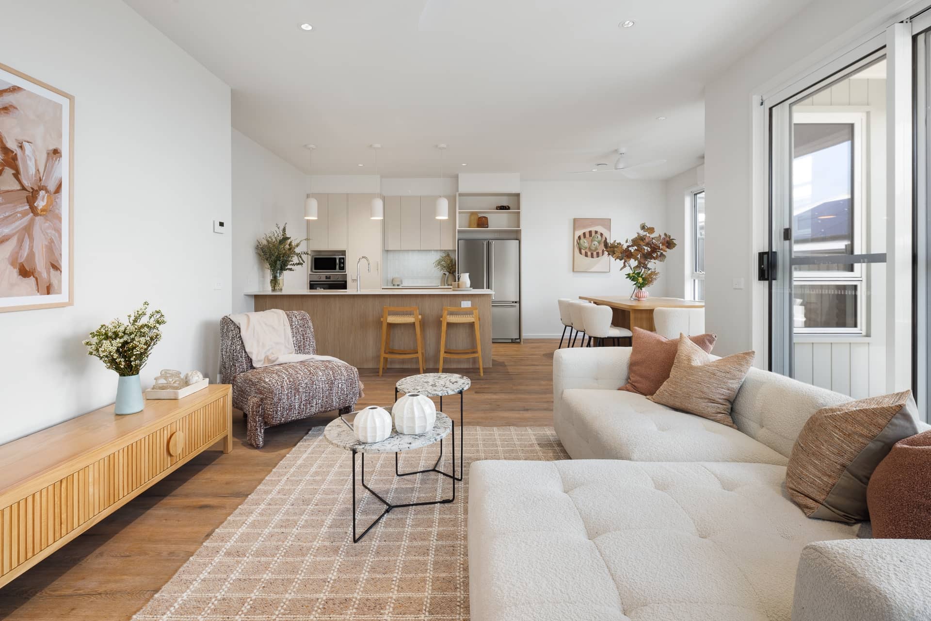 Modern open-plan living, dining, and kitchen in an Ingenia Lifestyle home, featuring neutral decor, wooden floors, a white sofa, and island bench.