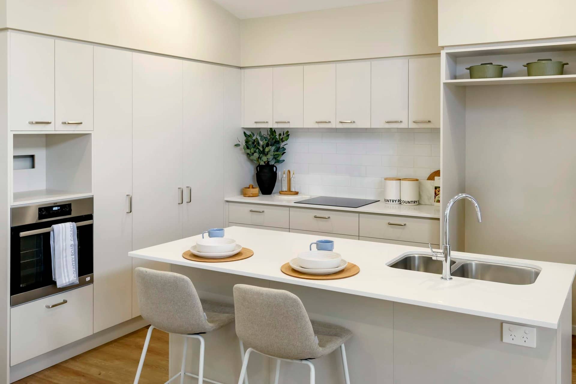 Modern kitchen island with two stools, set with plates and cups. Ingenia Lifestyle.