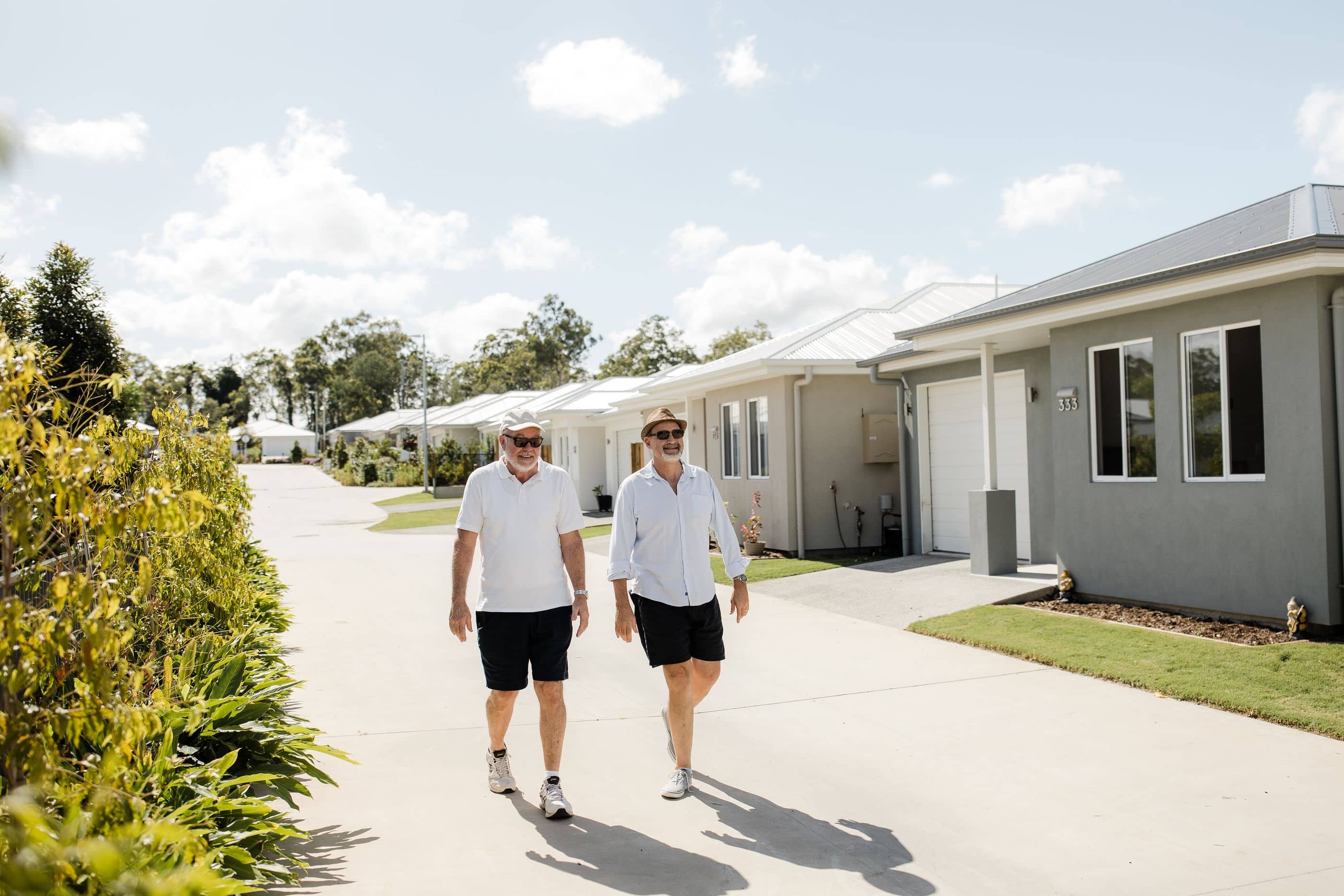 Two men walking down a paved path in an Ingenia Lifestyle community, with low-maintenance homes and landscaped grounds.