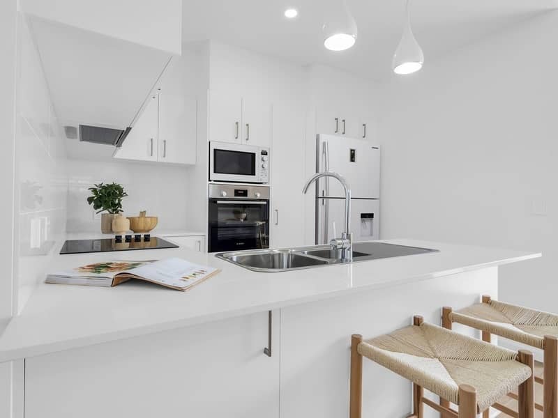 Modern white kitchen with island, double sink, chrome tap, microwave, oven and refrigerator.