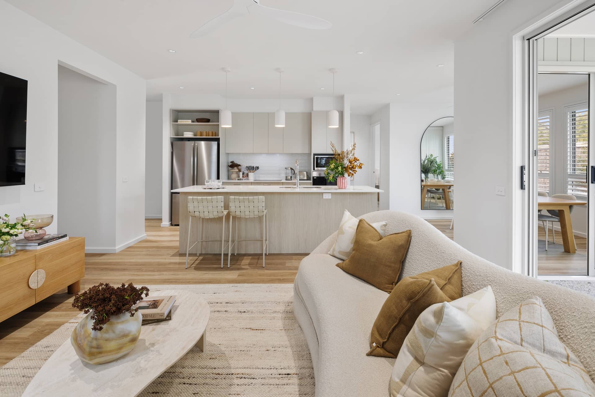 Modern open-plan living area with kitchen and dining spaces, featuring a curved sofa and light timber floors.