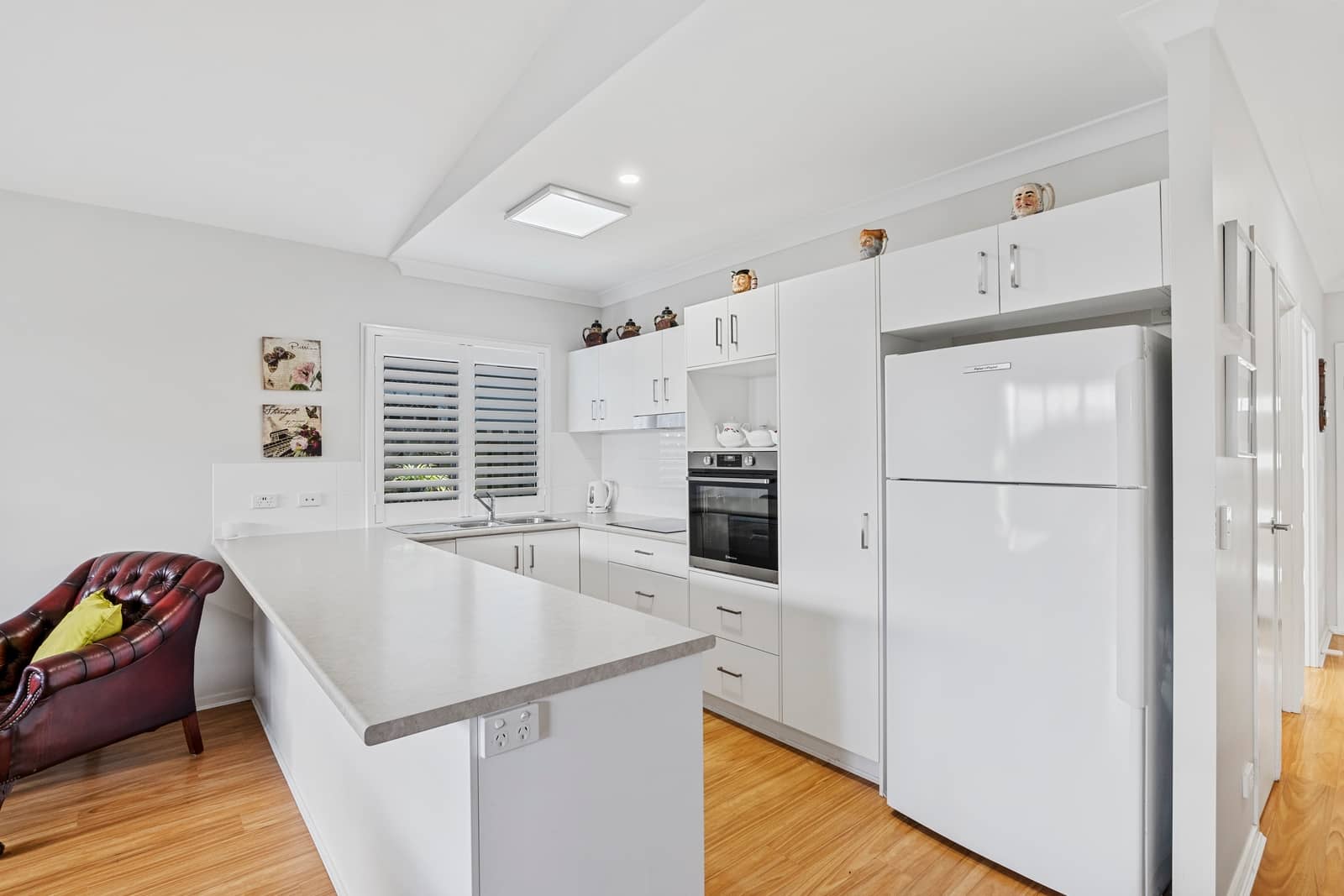 A modern kitchen with white cabinetry, stone benchtops, and a large white refrigerator.