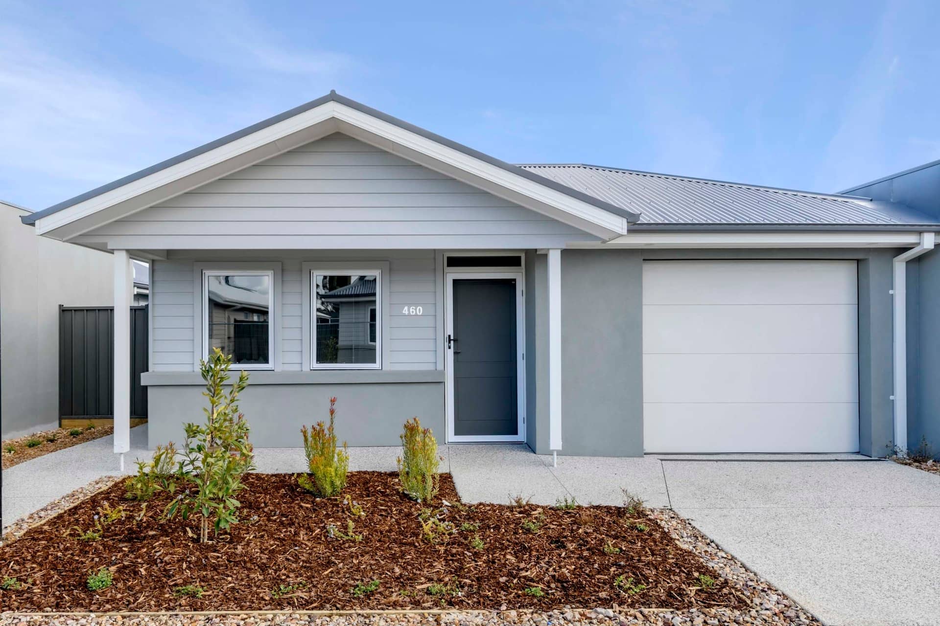 A modern Ingenia Lifestyle home with a grey exterior, white garage door, and landscaped garden.