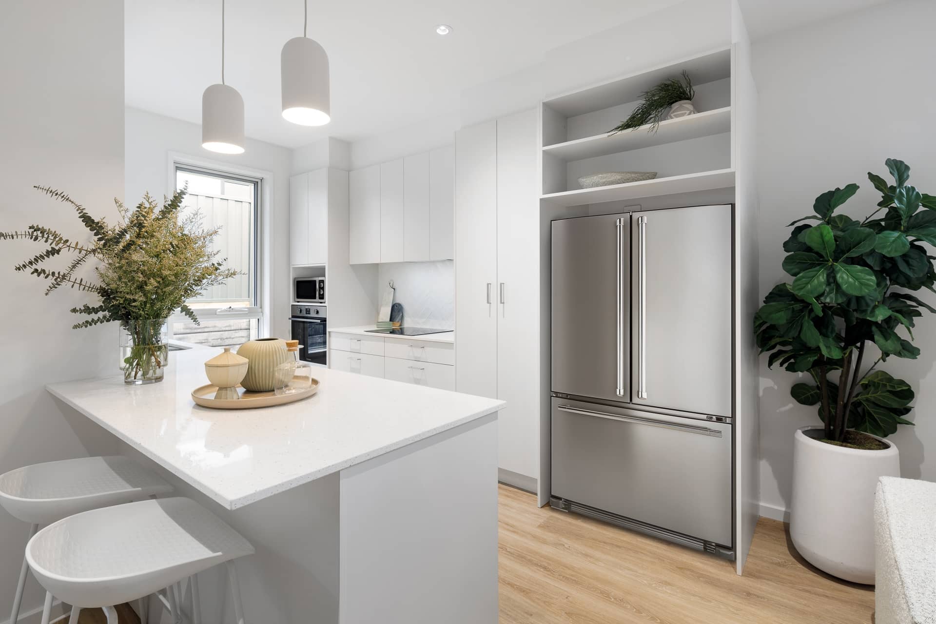 Modern white kitchen with stainless steel appliances, kitchen island with stools, and wood-look flooring in an Ingenia Lifestyle home.