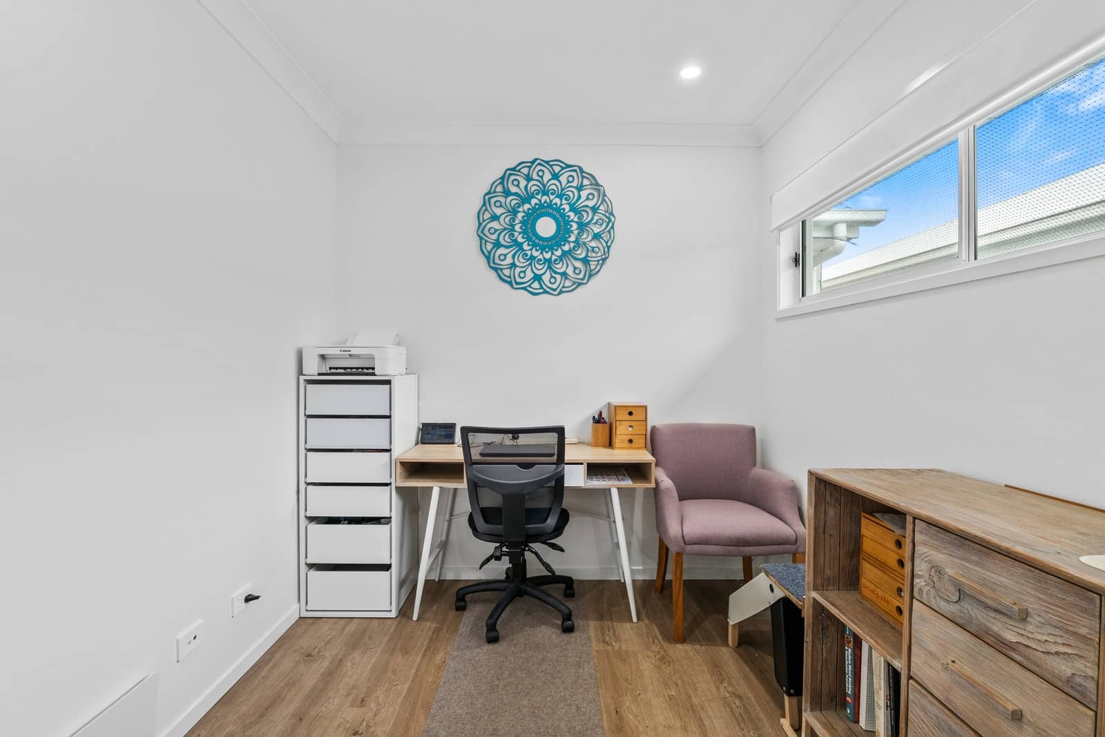 A modern home office in an Ingenia Lifestyle home with a wooden desk, office chair, storage units, and window.