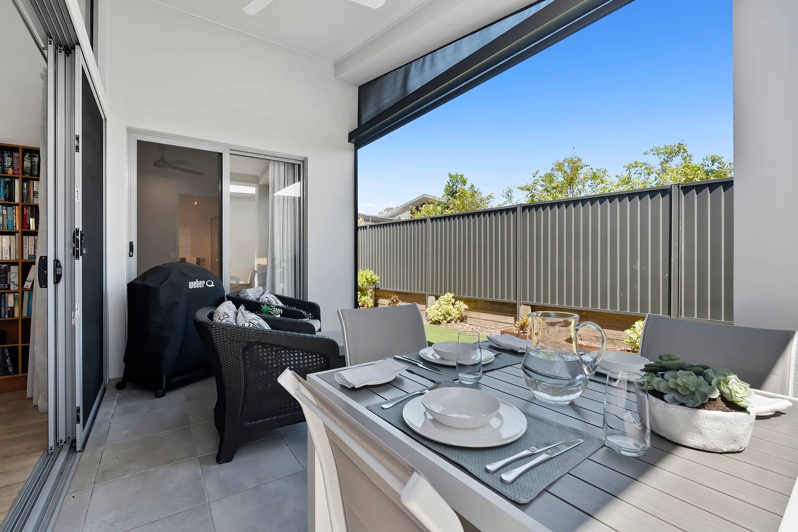 An outdoor patio of an Ingenia Lifestyle land lease home, featuring a dining table, seating, and BBQ, opening to a low-maintenance backyard.