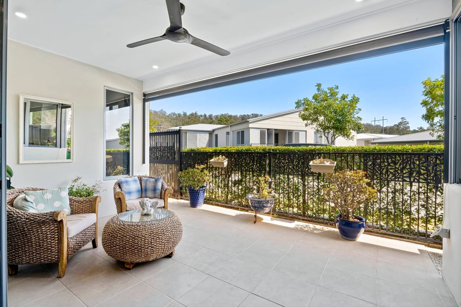 Covered outdoor patio with wicker seating and a ceiling fan, offering a view of other Ingenia Lifestyle homes.